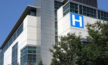 A multi-story hospital building displays a large, blue 