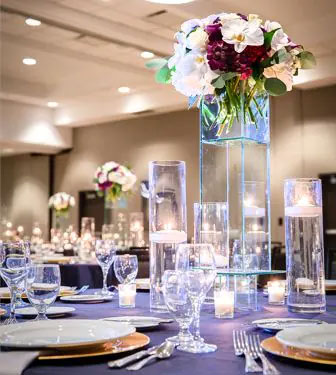 Several place settings with tall crystal centerpieces, containing a bouquet of red, white and green flowers