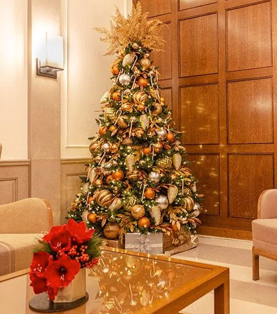 A majestically decoreated Christmas tree, stuffed with glistening ornaments and golden pine cones, stands in the seating area of a hotel lobby